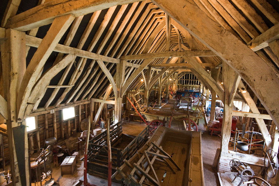 A large wooden-beamed barn with agricultural machines and equipment inside.